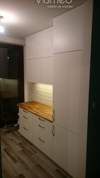 Kuchnia na dwie strony. Białe szafki lakierowane i drewniany blat